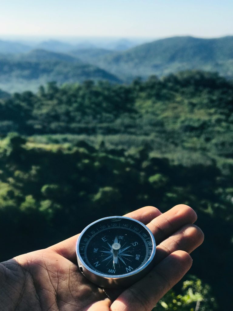 pexels-photo-1736222-1736222 A handheld compass over majestic green mountains under blue skies, ideal for travel themes.